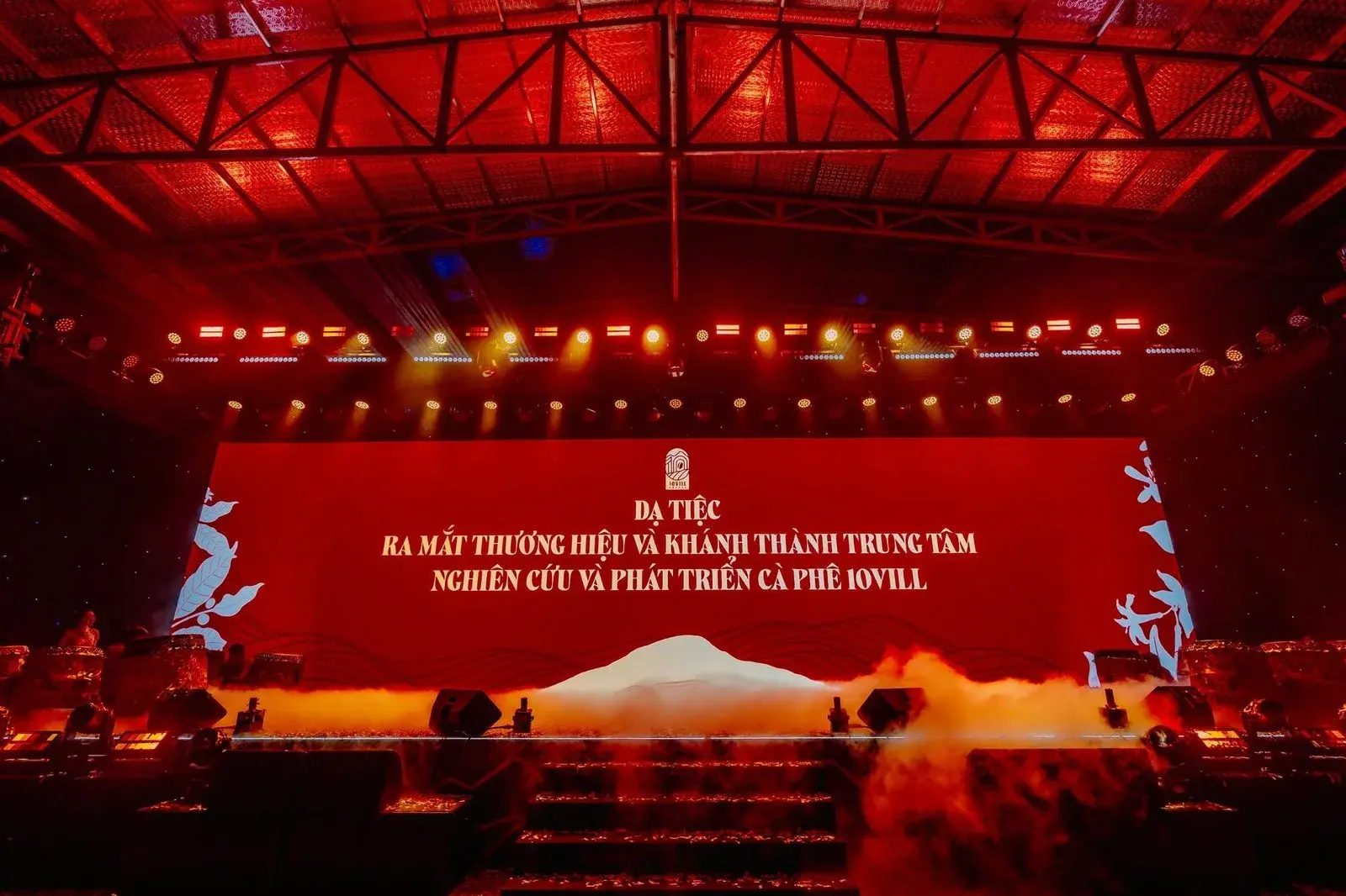 The launch gala from the back of the hall, the stage lit red under a wide LED wall