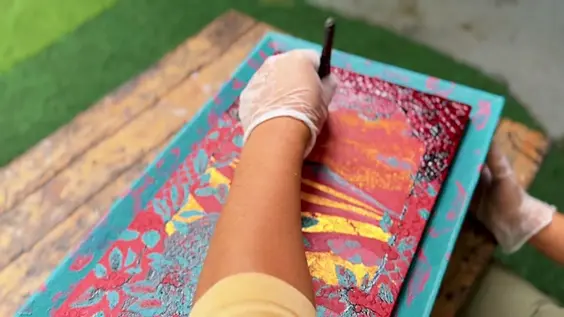A gloved hand painting the lid, brush loaded with vermilion