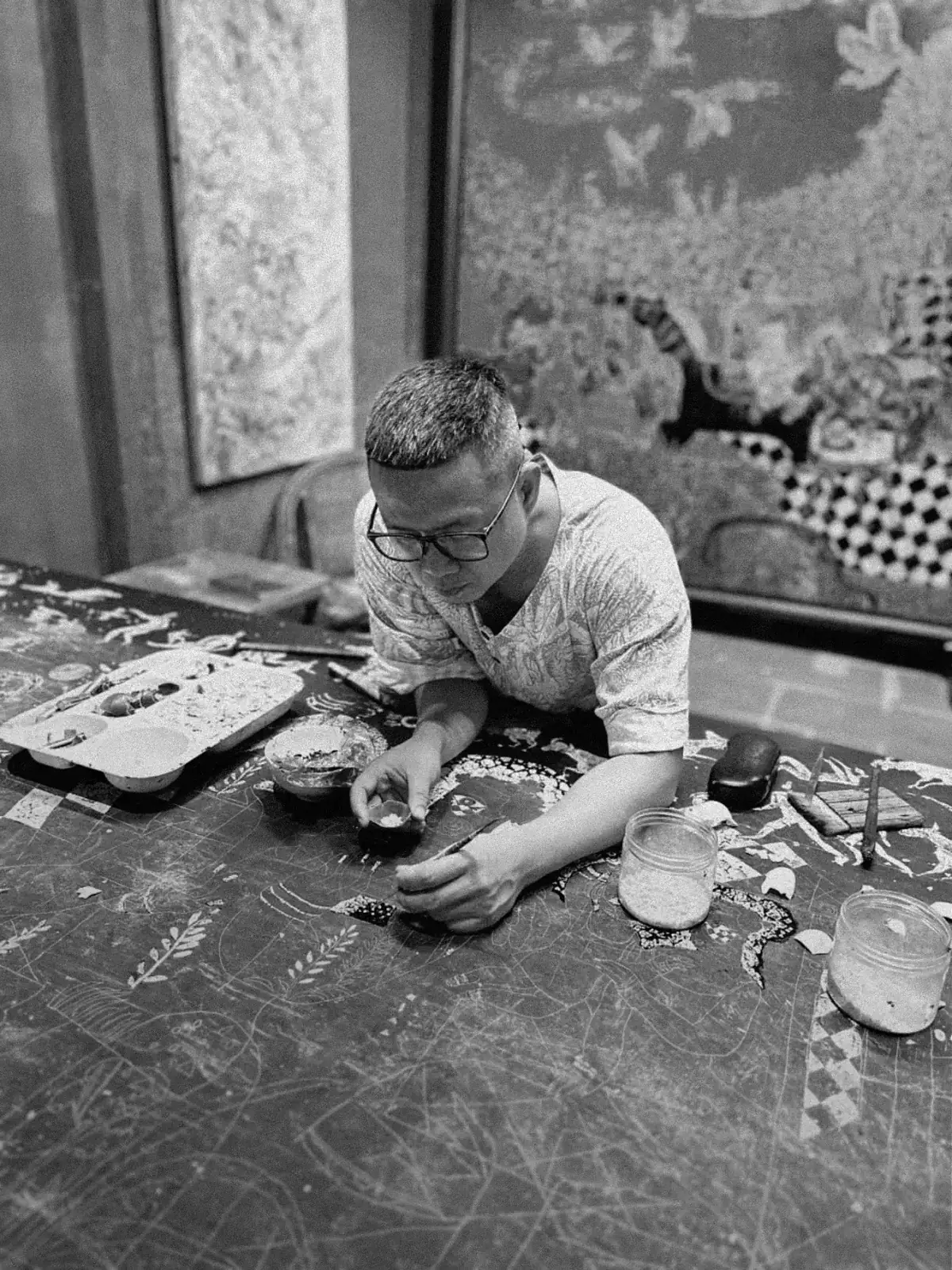 The artist working on the panel in his studio, tools laid out around him