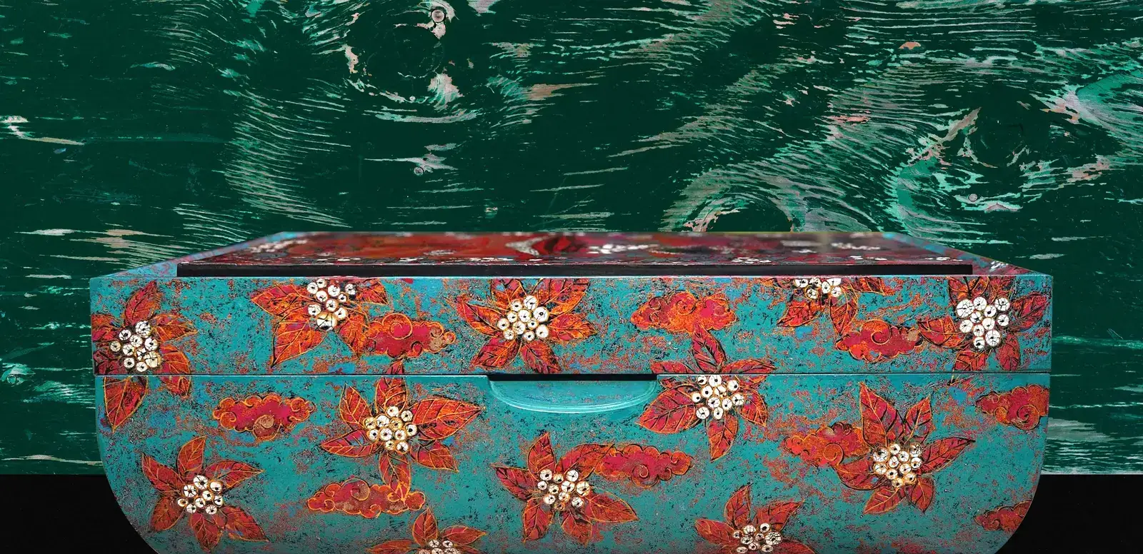 The lid seen edge-on — vermilion lacquer over a turquoise ground, eggshell blossom across the surface