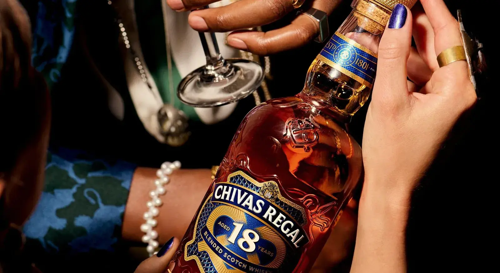 Hands pouring from the Chivas Regal 18 bottle at a party table
