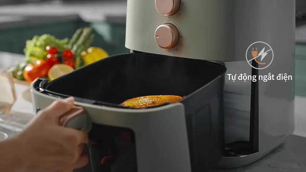 A hand lifting the fryer basket out over a pan of vegetables