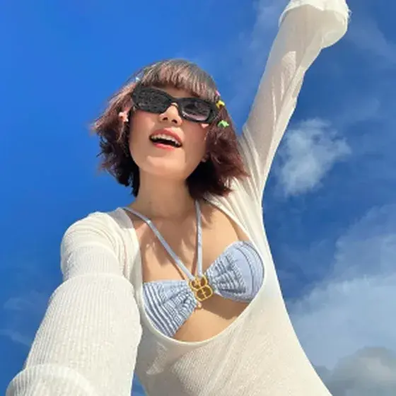 Creator portrait — a woman in sunglasses laughing against a blue sky