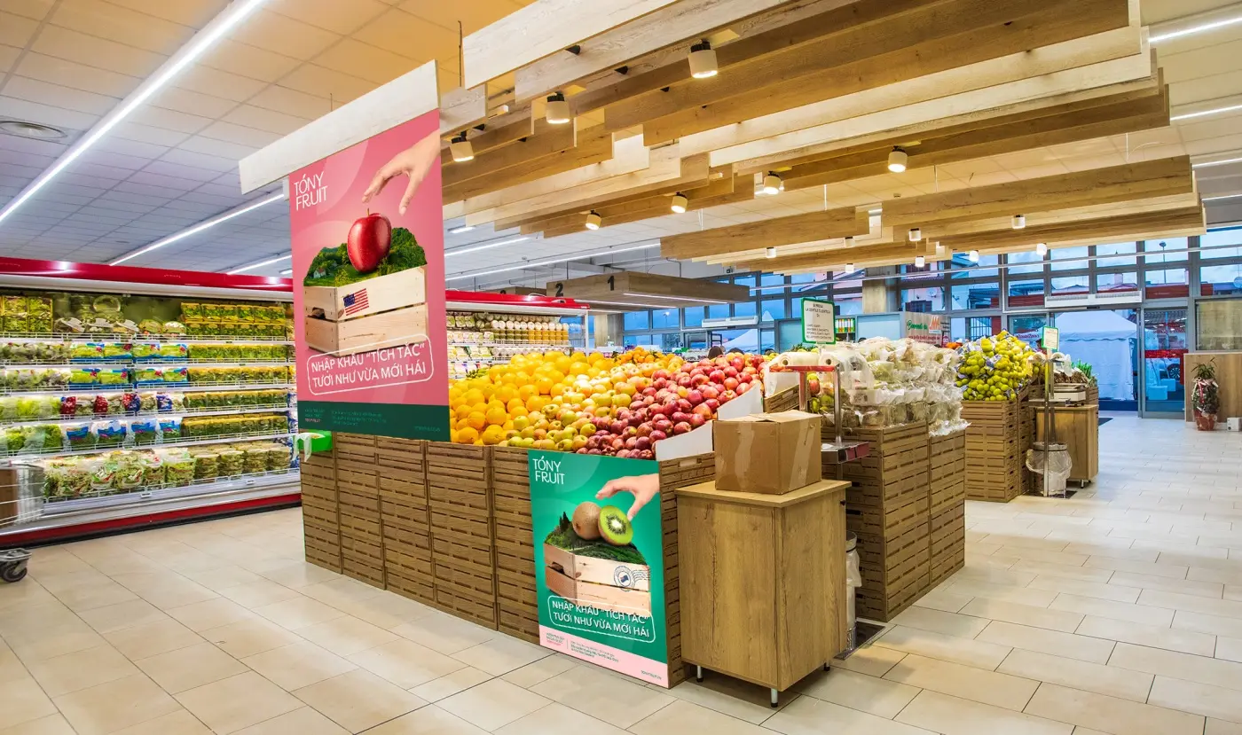 A supermarket produce aisle with branded crates and headers